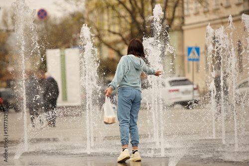A woman washes her hand in a fountain with a dry basin. Rest in a public place. Recreational design. Water resources of the city