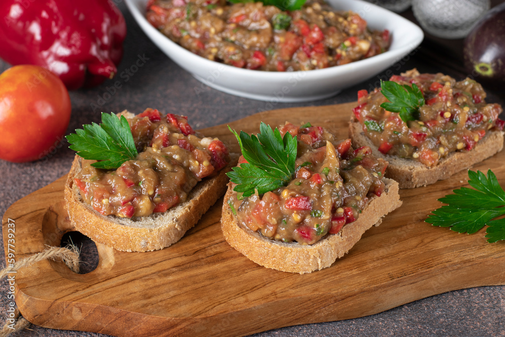 Homemade eggplant caviar with pepper, tomato and garlic on bread toasts on wooden board, Close up