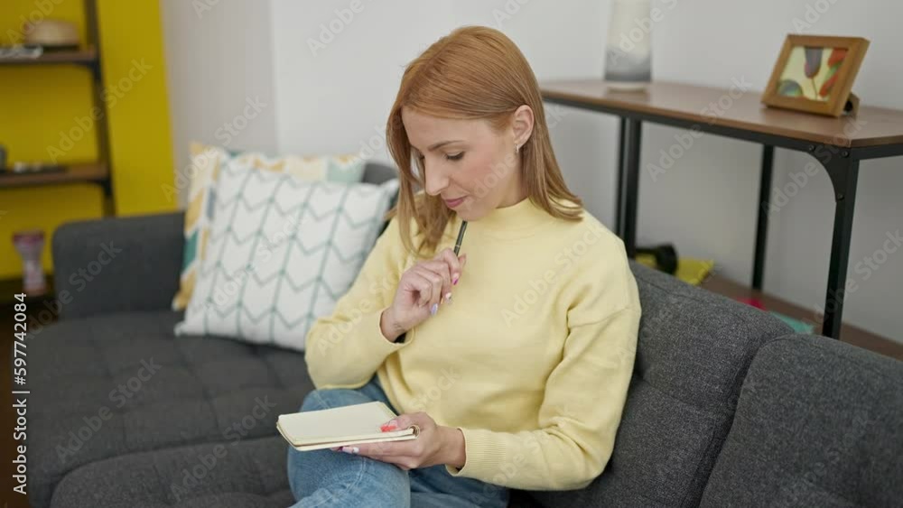 Young blonde woman writing on notebook sitting on sofa at home Young blonde woman writing on notebook sitting on sofa at home