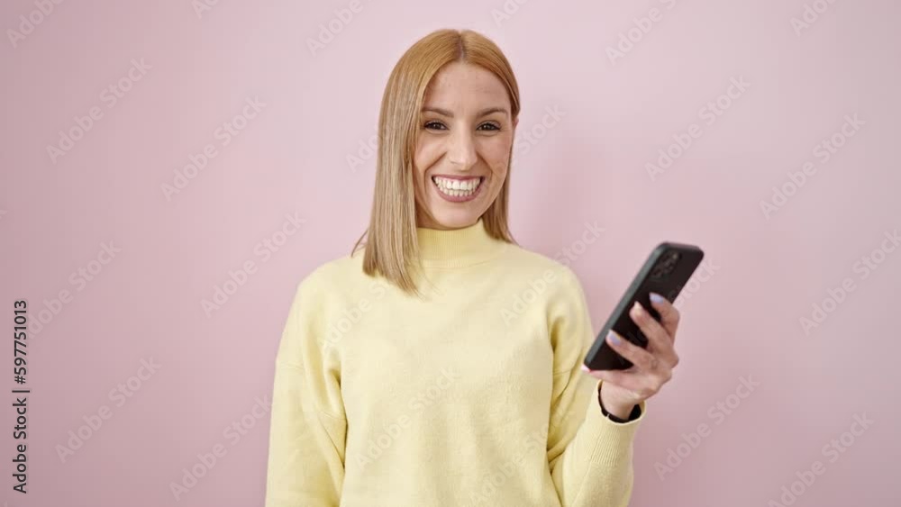 Young blonde woman using smartphone holding dollars over isolated pink background Young blonde woman using smartphone holding dollars over isolated pink background