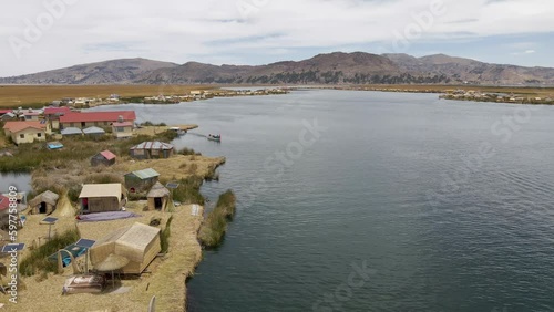 4K Aerial Drone Stationary view of boat carrying reeds at Uros Islands at Lake Titicaca, Puno, Peru. Lake, City, and Floating Islands visible