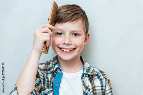 Foto Portrait of child combing hair with comb on gray studio background