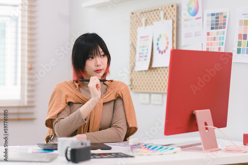 A creative female graphic designer is concentrating on the computer screen to design, code, and program a mobile application from a prototype and wireframe layout in the office.