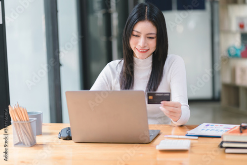 Cropped shot of female using laptop and hand holding black credit card mockup at workplace. Selective focusing © kenchiro168