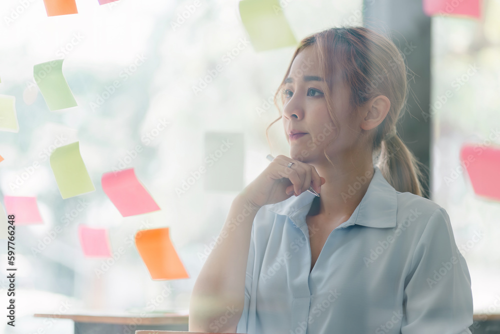The concept of brainstorming is exemplified as a focused and creative millennial Asian businesswoman shares ideas using sticky notes, placing them on a glass wall and engaging in deep thought. The concept of brainstorming is exemplified as a focused and creative millennial Asian businesswoman shares ideas using sticky notes, placing them on a glass wall and engaging in deep thought.