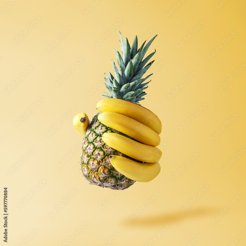 Fototapeta Creative fruit concept. Hand in the form of bananas holding a pineapple.