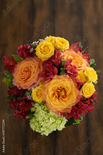 A beautiful arrangement of warm-colored roses taken from above on a brown wooded dining table.