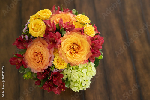 On a brown table background, a beautiful floral arrangement of orange, yellow, and red flowers with free space for text.