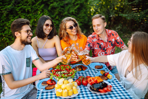 Group of young friends gathered in garden for picnic. Friends have fun, communicate in nature, drink beer. Company gathered for barbecue. Concept of vacation, lifestyle, vacation.