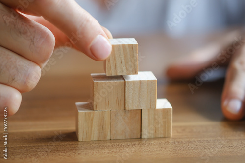 Close-up photo of man putting wooden block on top of pyramid. Planning business growth. Horizontal concept with copy space for your text