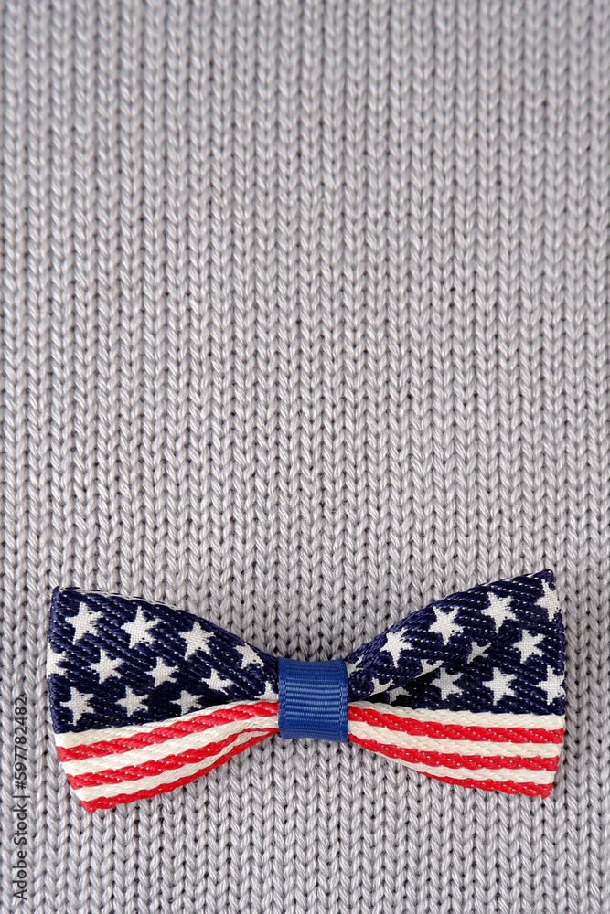 Obraz premium Bow tie with the image of the US flag on a gray knitted background.For the design of postcards, banners in clothing stores and accessories for national holidays.Independence Day.Vertical photo