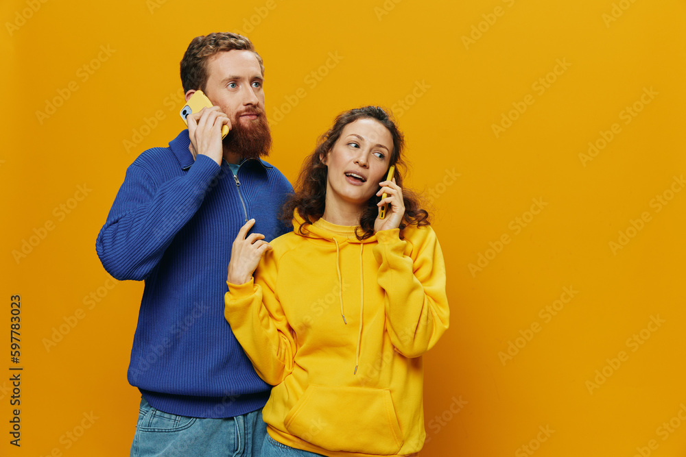 Naklejka premium Man and woman couple smiling merrily with phone in hand social media viewing photos and videos, on yellow background, symbols signs and hand gestures, family freelancers.