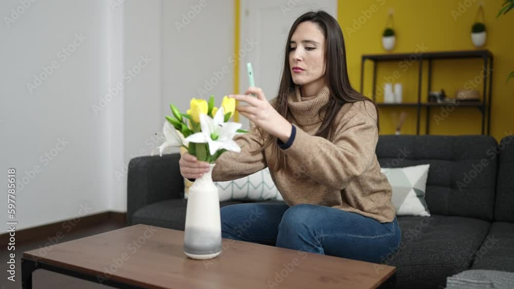 Beautiful hispanic woman taking picture of flowers in a vase sitting on the sofa at home Beautiful hispanic woman taking picture of flowers in a vase sitting on the sofa at home