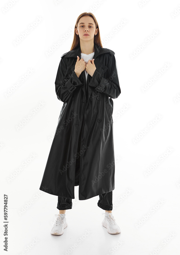 Fashion young beautiful model in long leather coat and dark jeans on white background. Fashion young beautiful model in long leather coat and dark jeans on white background.