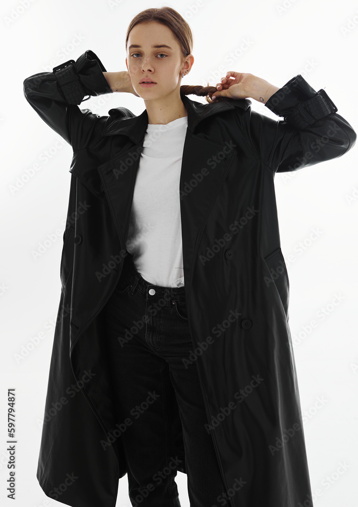 Fashion young beautiful model in long leather coat and dark jeans on white background. Fashion young beautiful model in long leather coat and dark jeans on white background.