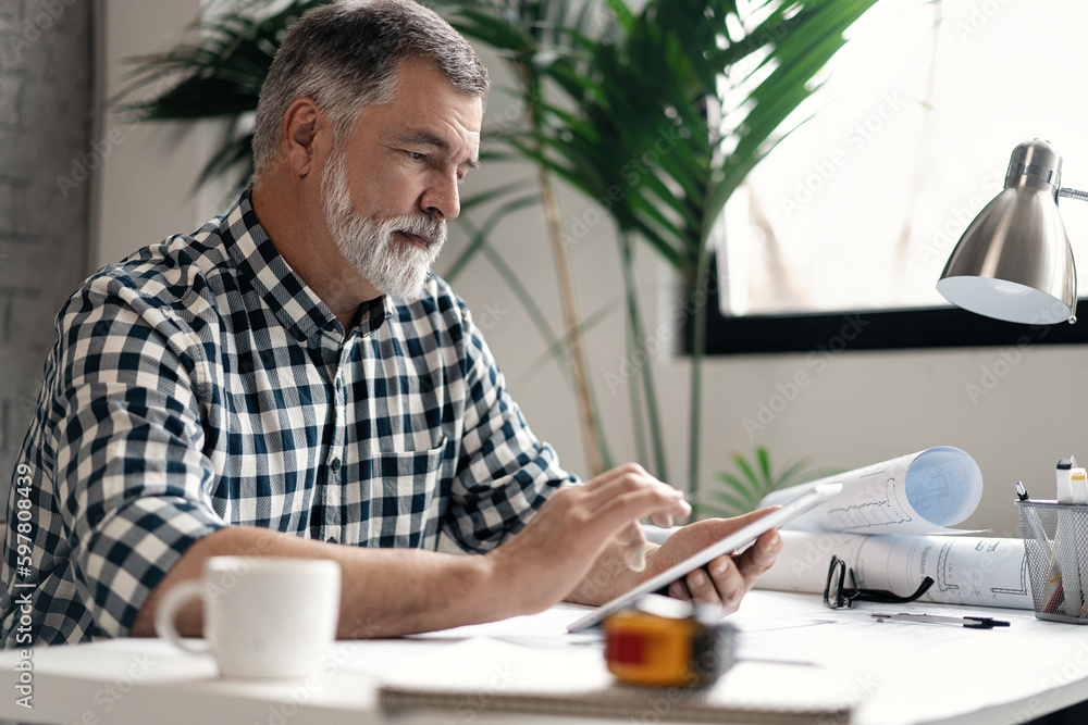 Mature confident smiling architect in casual wear working with blueprint papers and drawings in modern lightful office. Mature confident smiling architect in casual wear working with blueprint papers and drawings in modern lightful office.