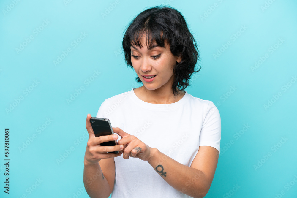 Young Argentinian woman isolated on blue background sending a message or email with the mobile Young Argentinian woman isolated on blue background sending a message or email with the mobile