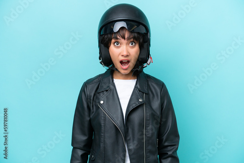 Young Argentinian woman with a motorcycle helmet isolated on blue background looking up and with surprised expression © luismolinero