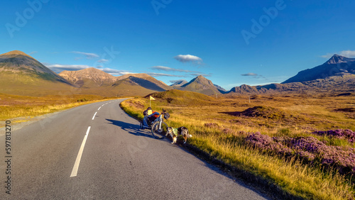 Hund steht mit Fahrrad auf Straße mit Blick auf Berge auf der Insel Skye © iris