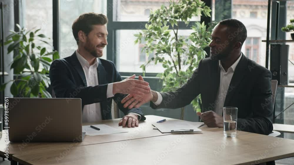 Two diverse businessmen at office meeting shake hands after successful business contract agreement. African businessman signing paper document offer Caucasian man salesman handshake client customer