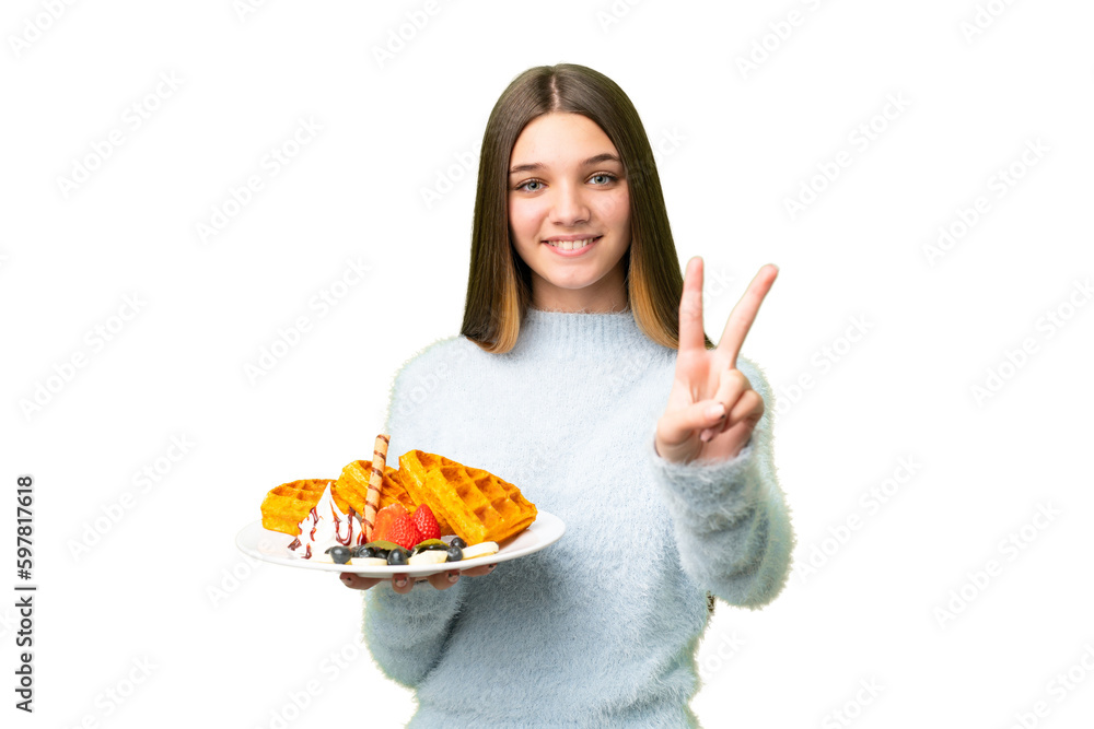 Teenager girl holding waffles over isolated chroma key background smiling and showing victory sign Teenager girl holding waffles over isolated chroma key background smiling and showing victory sign