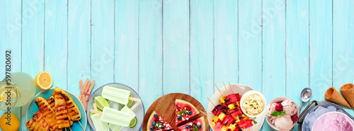 Refreshing summer food bottom border. Selection of grilled fruits, ice cream and ice pops. Top view on a blue wood banner background.