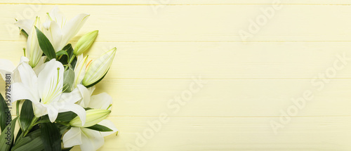 Beautiful lily flowers on yellow wooden background with space for text