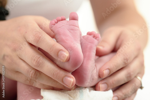 HOUSTON, TEXAS - APRIL 26TH 2023: a newborn baby’s tiny pink feet are photographed close up in their mother’s hands to compare the size. You can see every detail and line on the skin.