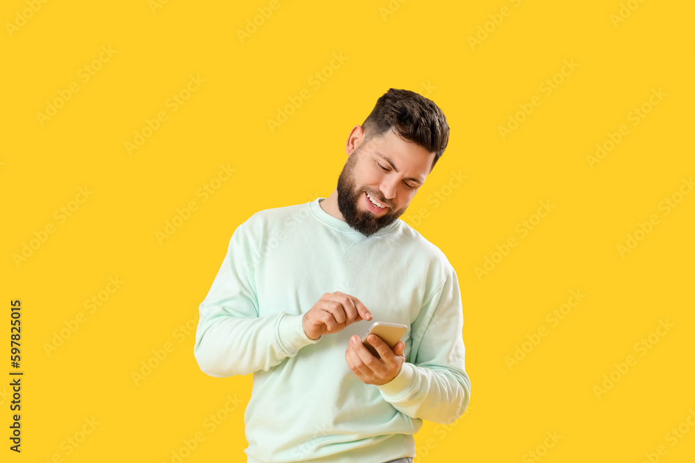 Young bearded man using mobile phone on yellow background Young bearded man using mobile phone on yellow background