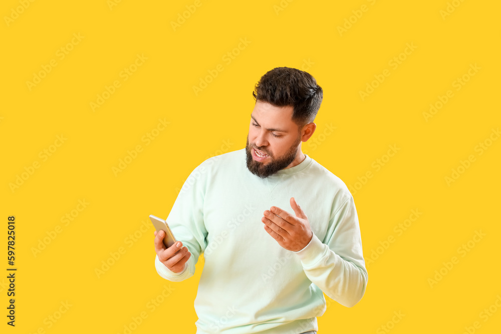 Young bearded man using mobile phone on yellow background Young bearded man using mobile phone on yellow background