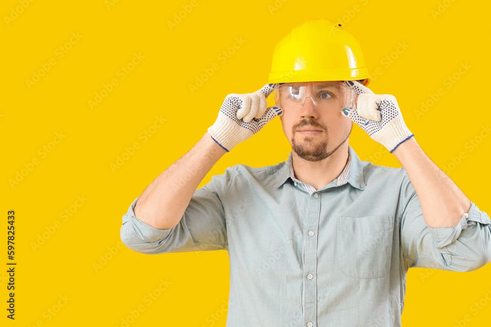 Male carpenter in safety goggles on yellow background Male carpenter in safety goggles on yellow background