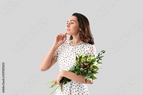 Young woman in dress with alstroemeria flowers on grey background