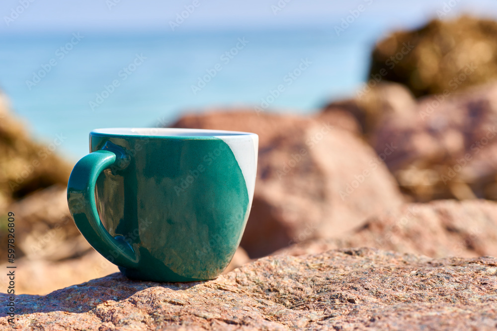 Green ceramic cups for coffee tea beverages on the shore of a rocky sea bay Green ceramic cups for coffee tea beverages on the shore of a rocky sea bay