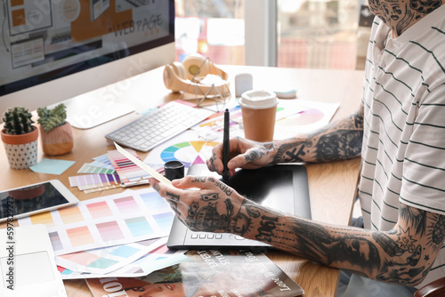 Tattooed graphic designer working with tablet and paint palette on table in office, closeup