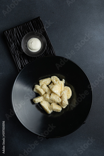 A bowl of gnocchi with a side of sour cream.