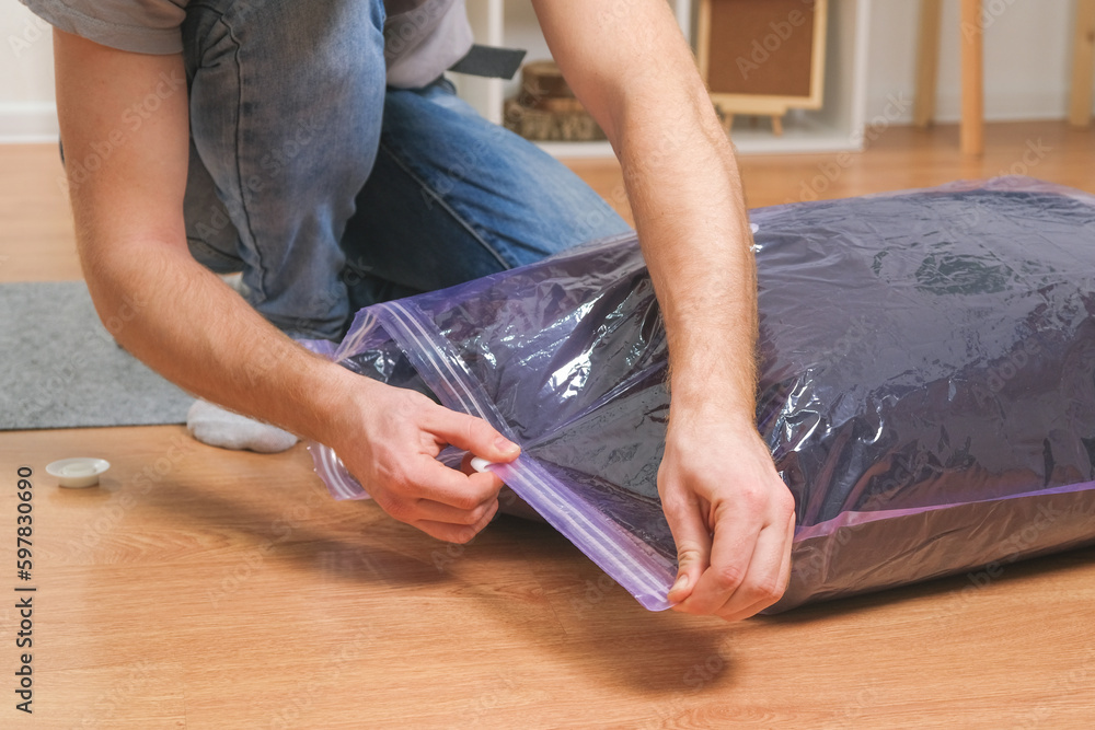 A man folds winter jackets and puts them in a vacuum bag for seasonal storage in the closet. Space saving and careful storage of clothes. Organization of storage.