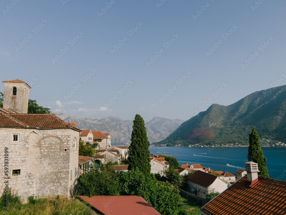 Old stone houses with red tiled roofs among green trees. Perast, Montenegro