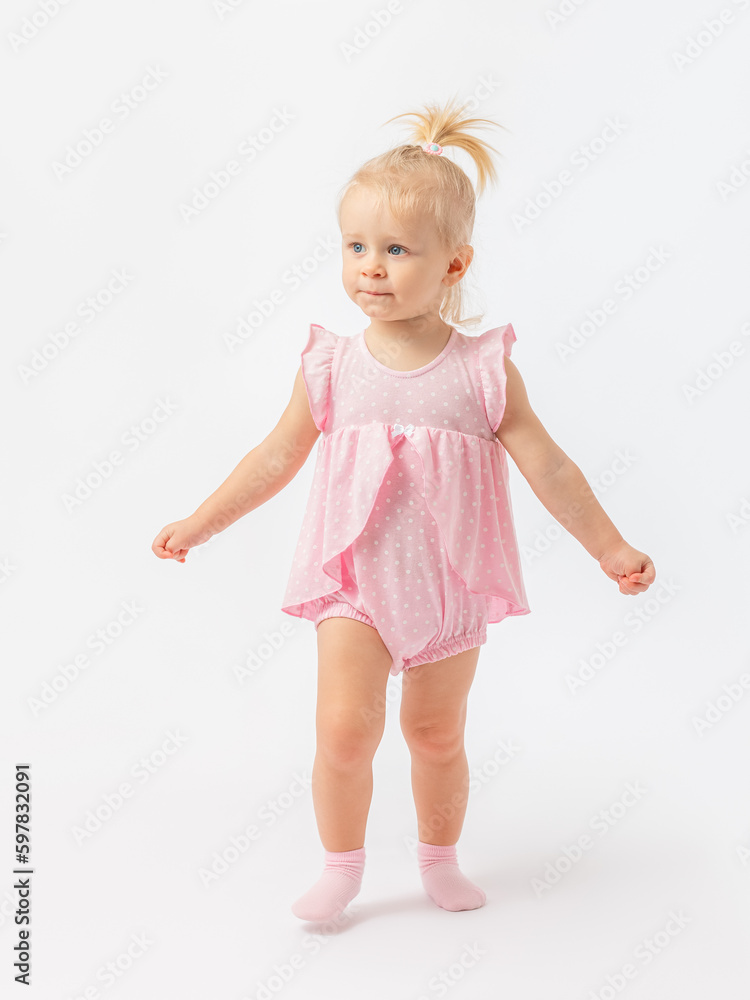 A cute 1-2-year-old girl in a pink dress in socks walks waving her hands on a white background. A cute 1-2-year-old girl in a pink dress in socks walks waving her hands on a white background.