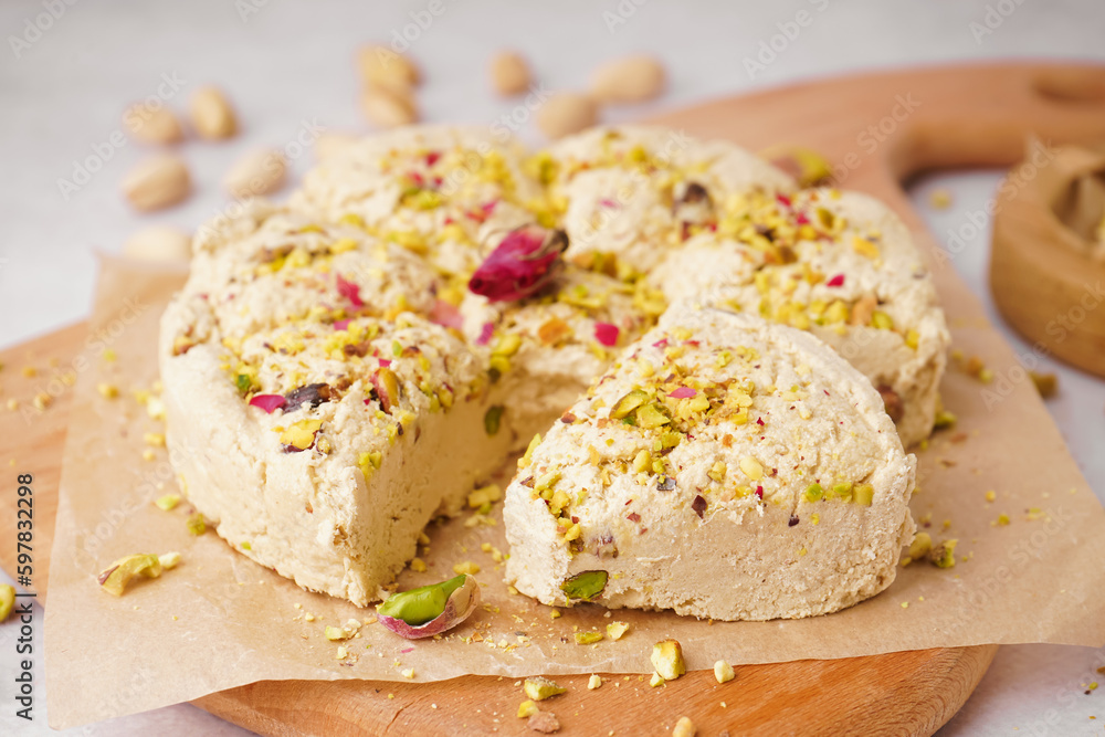 Wooden board of tasty Tahini halva with pistachios on light background, closeup