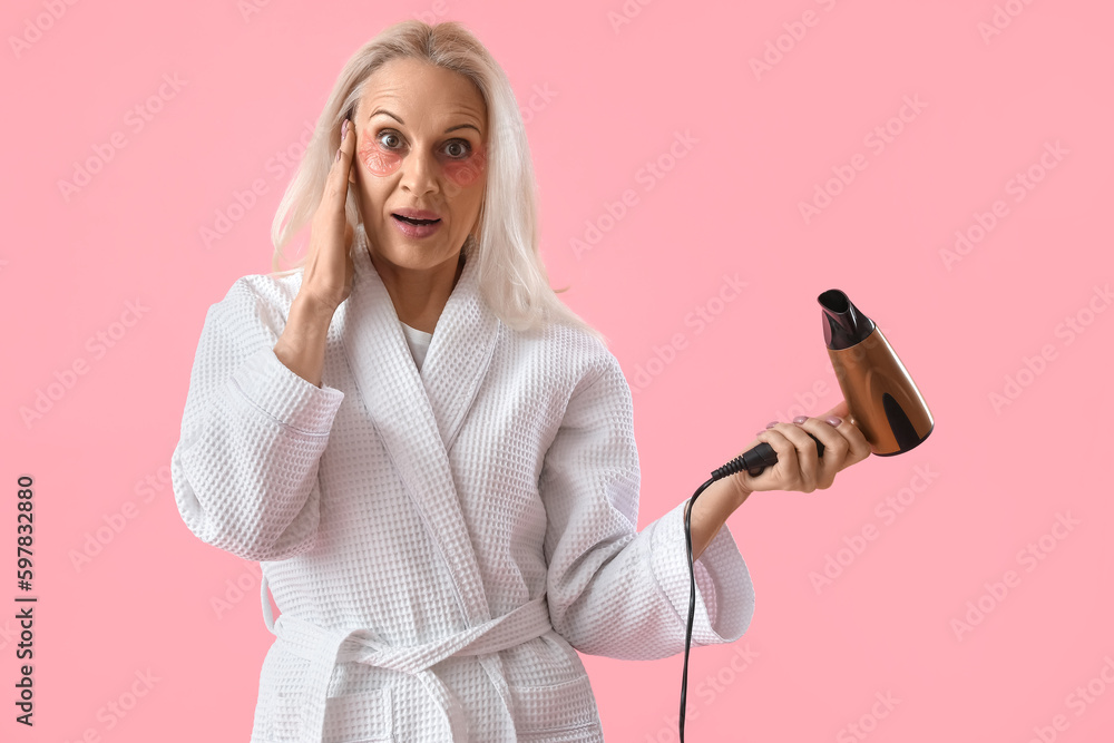Surprised mature woman with hair dryer on pink background Surprised mature woman with hair dryer on pink background