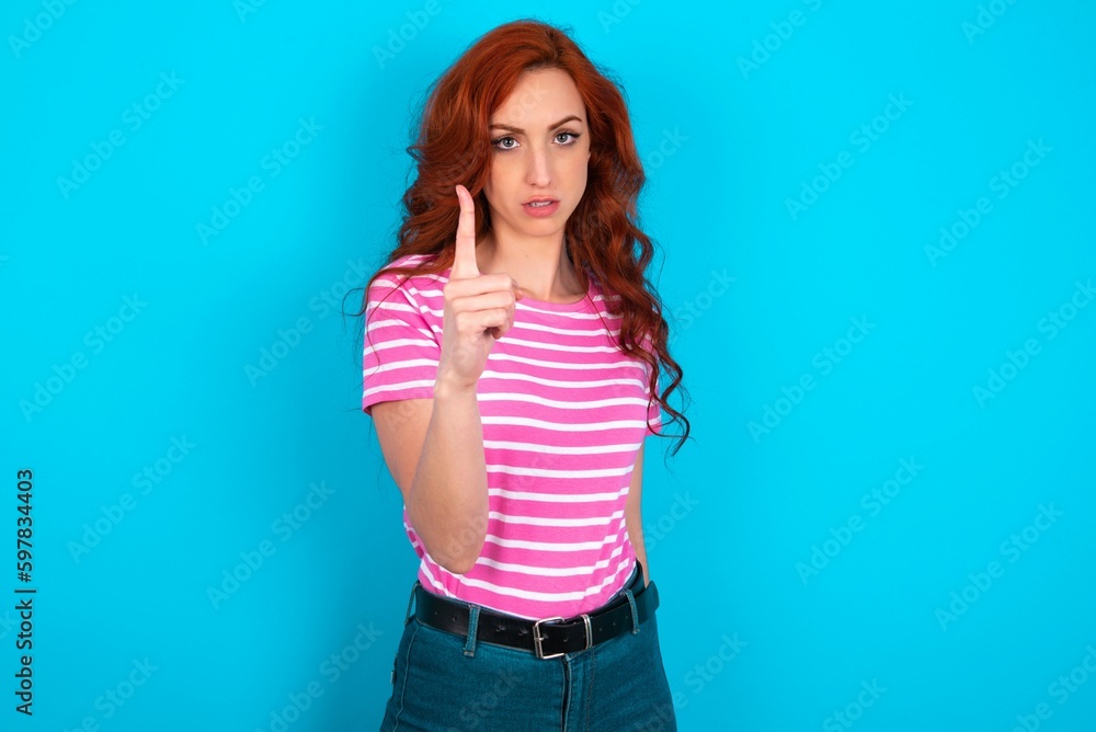 young redhead woman wearing striped T-shirt over blue background frustrated and pointing to the front young redhead woman wearing striped T-shirt over blue background frustrated and pointing to the front