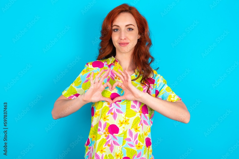 Serious Young redhead woman wearing colorful shirt over blue background keeps hands crossed stands in thoughtful pose concentrated somewhere Serious Young redhead woman wearing colorful shirt over blue background keeps hands crossed stands in thoughtful pose concentrated somewhere