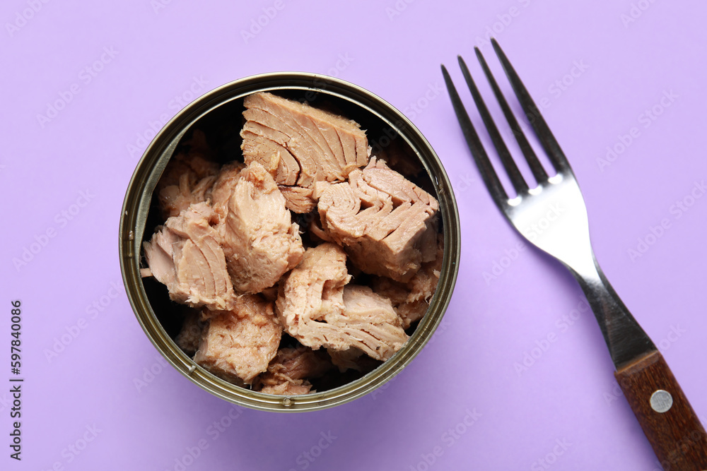 Opened tin can with delicious tuna and fork on lilac background Opened tin can with delicious tuna and fork on lilac background
