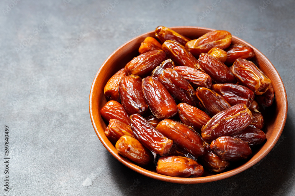 Pitted dates on a clay plate. Bowl with delicious dried dates on a dark background. Ramadan kareem. Top view. Copy space Pitted dates on a clay plate. Bowl with delicious dried dates on a dark background. Ramadan kareem. Top view. Copy space