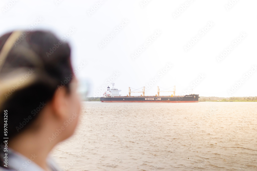 Cargo ship sailing on the Magdalena River while a woman is seen in the background, looking towards the ship