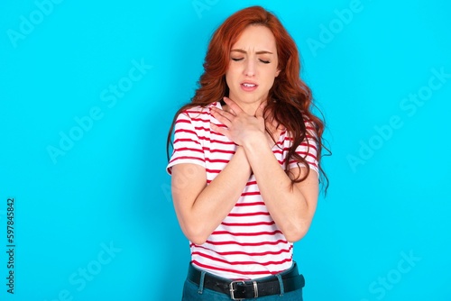 Photo young redhead woman wearing striped T-shirt over blue background shouting suffocate because painful strangle