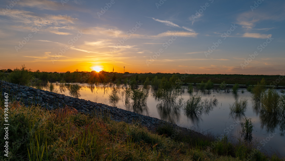 Sunset behind levee with high water next to levee flooding trees