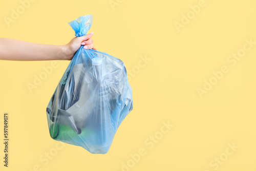 Female hand holding full garbage bag on yellow background photo