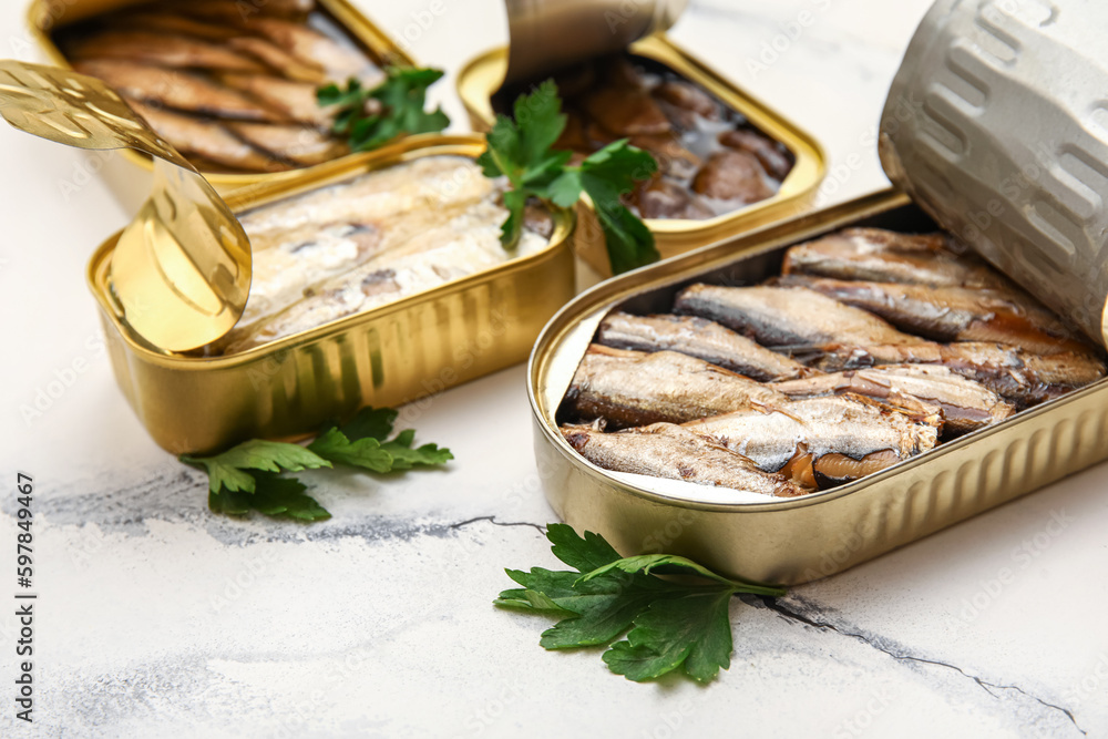 Opened tin cans with sprats in oil on white marble table Opened tin cans with sprats in oil on white marble table