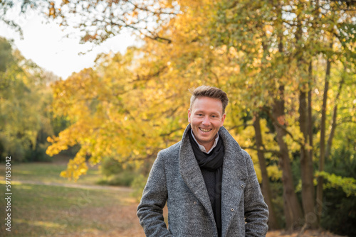 Beautiful causasian man posing during autumn in a park with the sun shining from behind. Berlin, Germany.